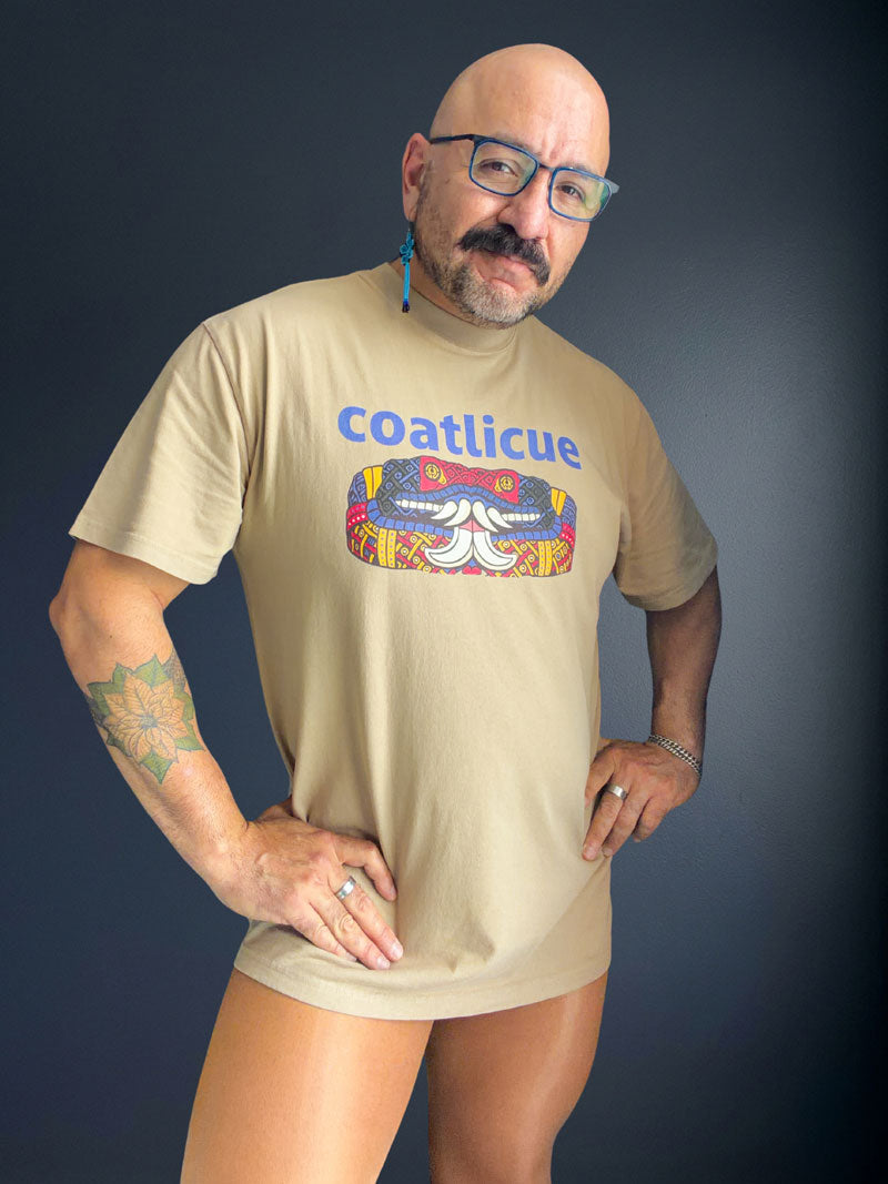 Cesar Torres in the faded khaki Coatlicue tee with both hands on the hips, showing the boxy oversized fit and dropped shoulders.