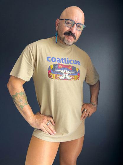 Cesar Torres in the faded khaki Coatlicue tee with both hands on the hips, showing the boxy oversized fit and dropped shoulders.
